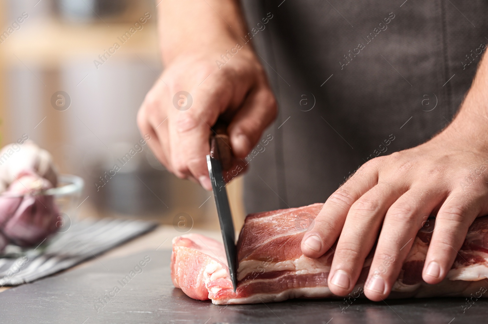 Photo of Man cutting fresh raw meat on table in kitchen, closeup