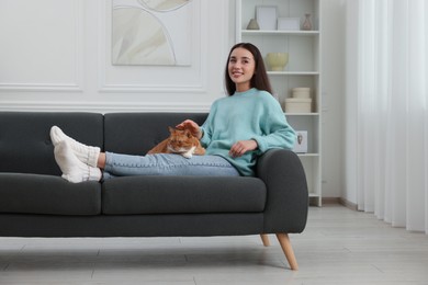 Beautiful woman petting cute cat on sofa at home