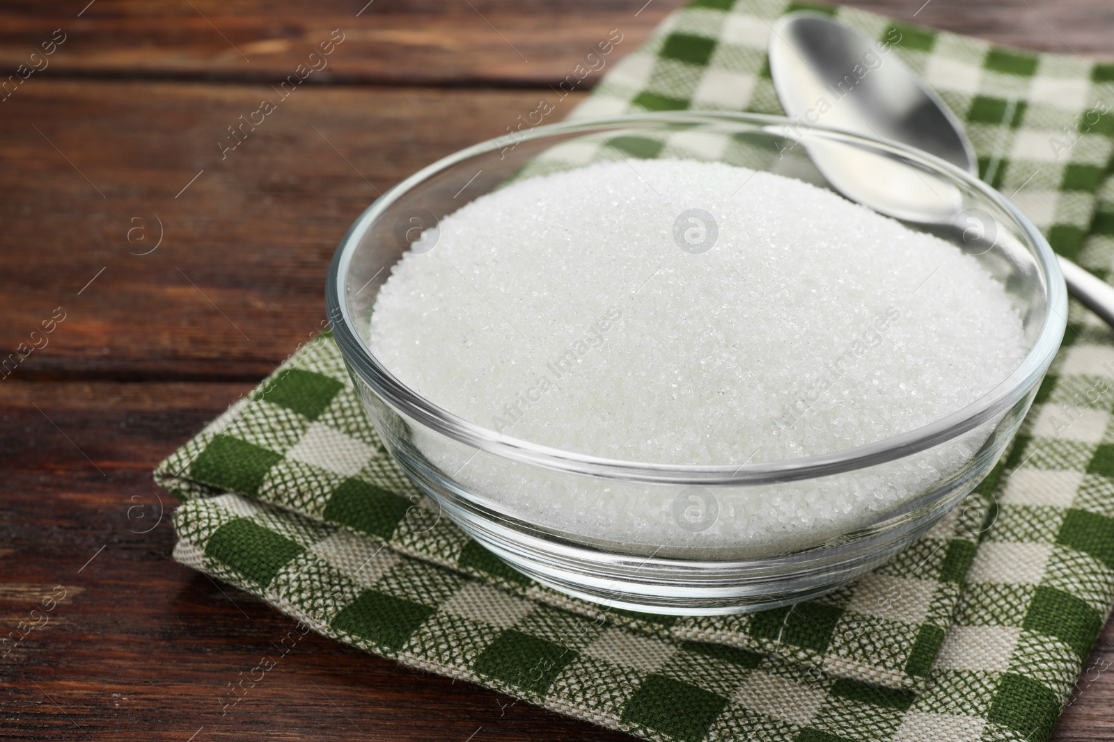 Photo of Granulated sugar in bowl and napkin on wooden table, closeup