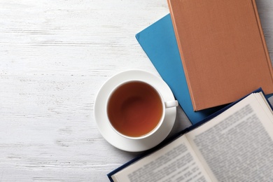 Hardcover books and cup of tea on white wooden table, flat lay