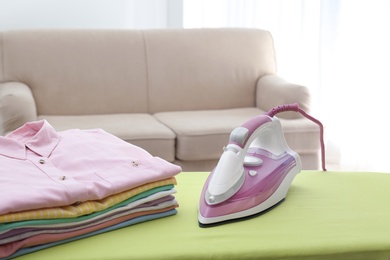 Photo of Board with modern iron and clean laundry at home