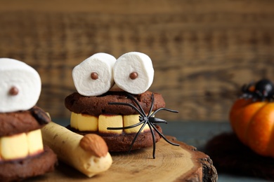 Photo of Delicious desserts decorated as monsters on stump, closeup. Halloween treat