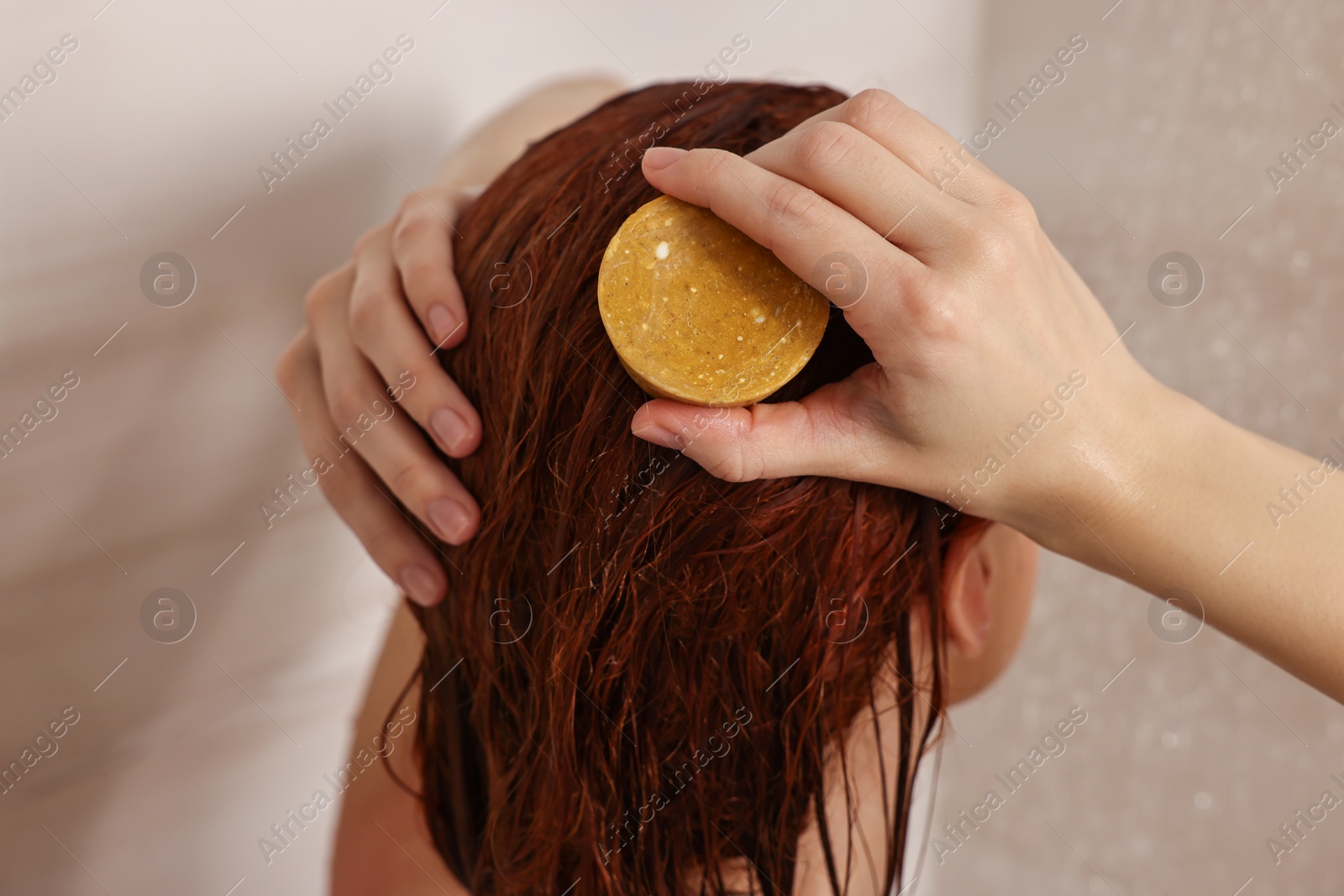 Photo of Young woman washing her hair with solid shampoo bar in shower, back view