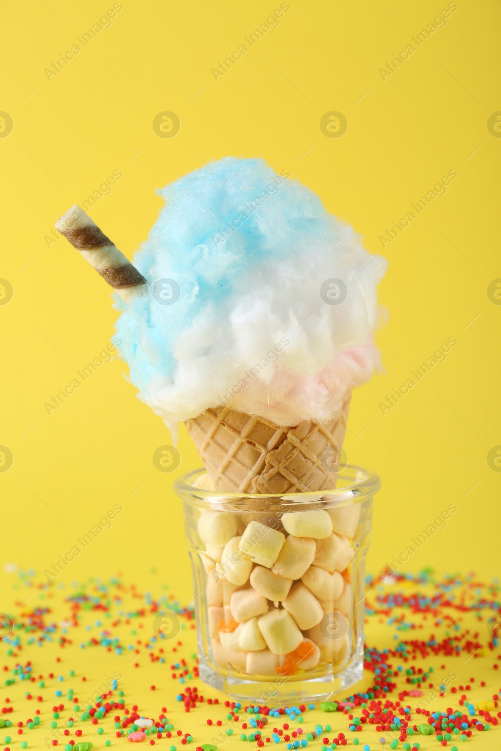 Photo of Sweet cotton candy in waffle cone on yellow background, closeup