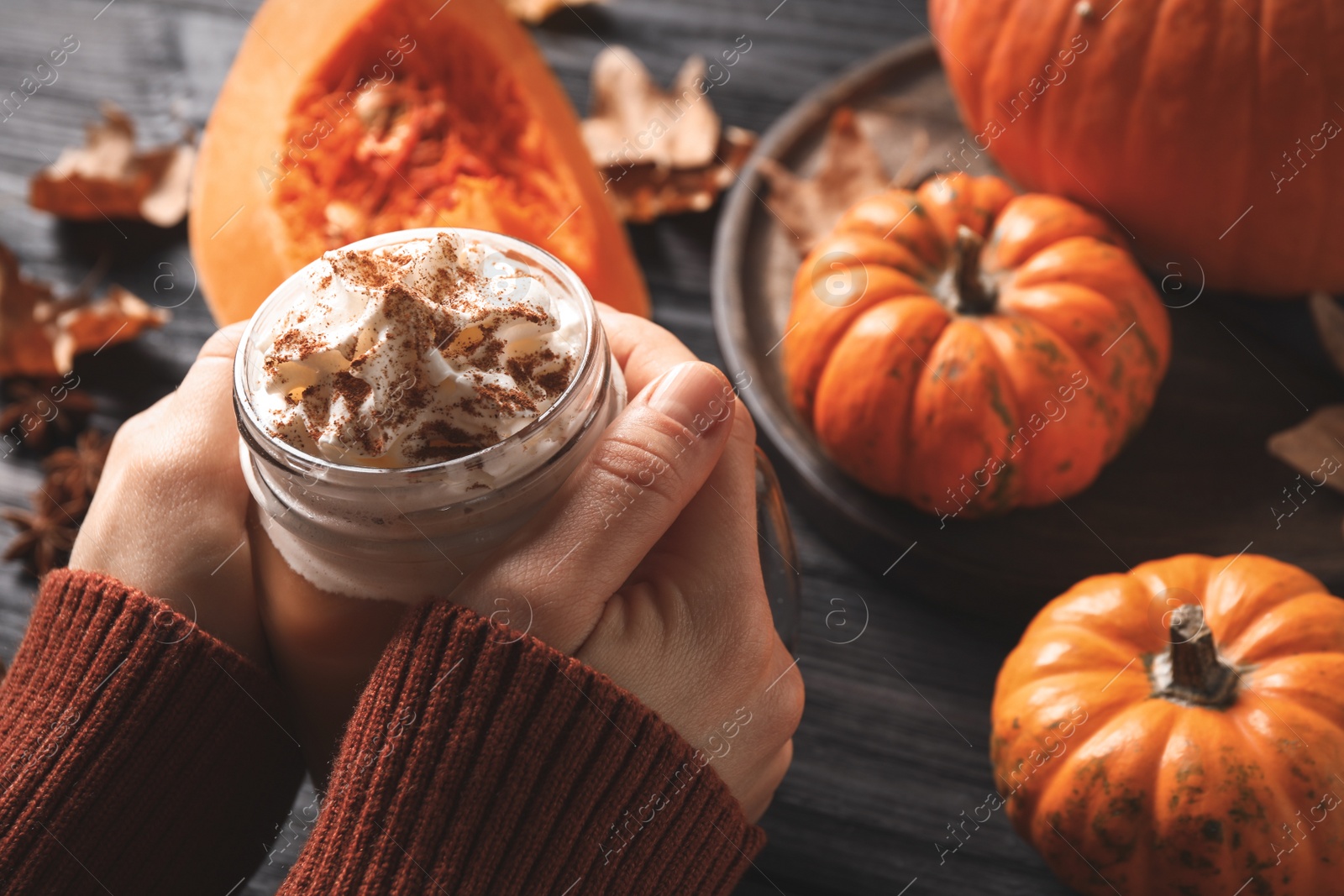 Photo of Woman holding tasty pumpkin latte at black wooden table, closeup