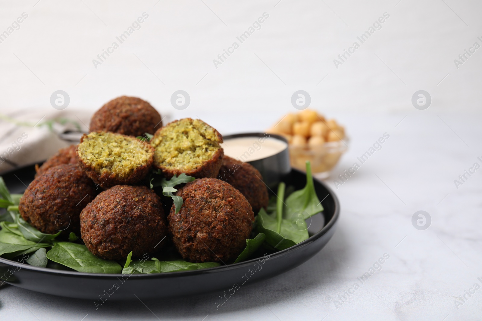 Photo of Delicious falafel balls, herbs and sauce on white marble table, closeup