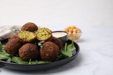 Photo of Delicious falafel balls, herbs and sauce on white marble table, closeup