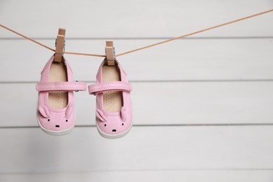 Photo of Pink baby shoes drying on washing line against white wall. Space for text