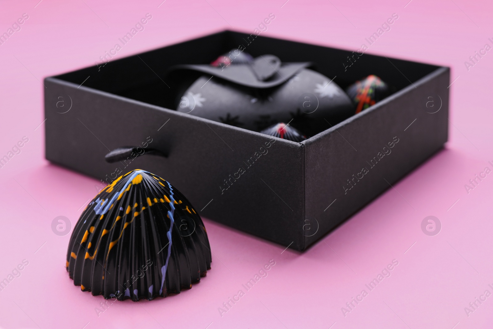 Photo of Tasty chocolate candy near open box on pink background, closeup