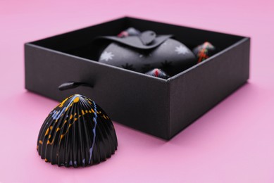 Photo of Tasty chocolate candy near open box on pink background, closeup