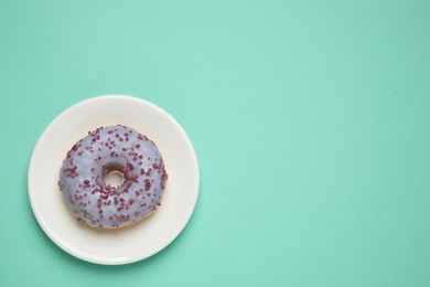Photo of Delicious glazed donut on turquoise background, top view. Space for text