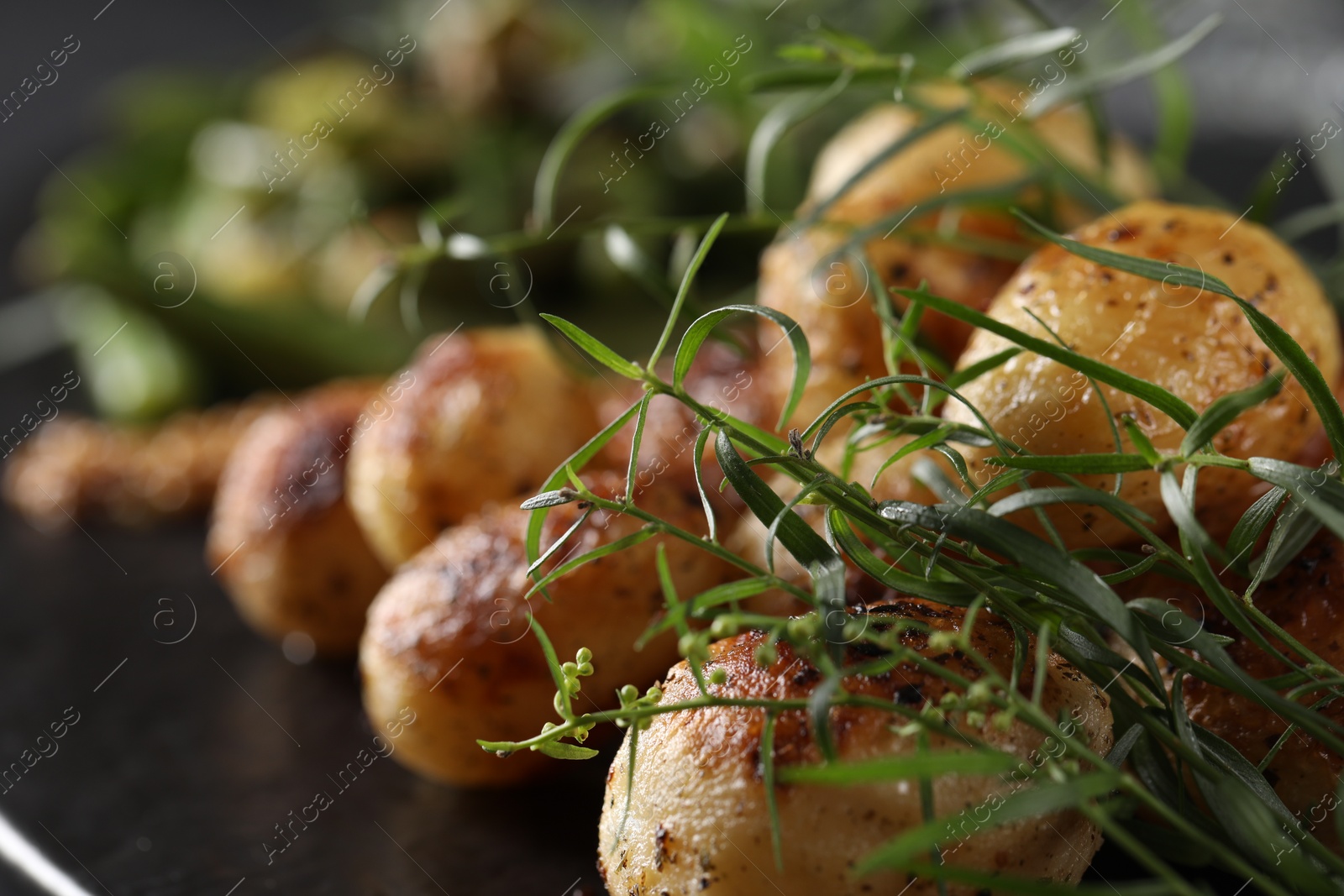 Photo of Delicious grilled potatoes with tarragon on black table, closeup