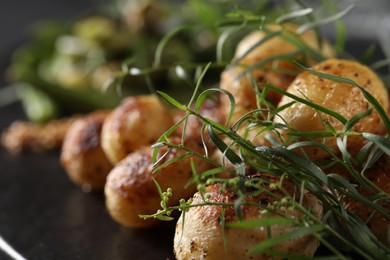 Delicious grilled potatoes with tarragon on black table, closeup