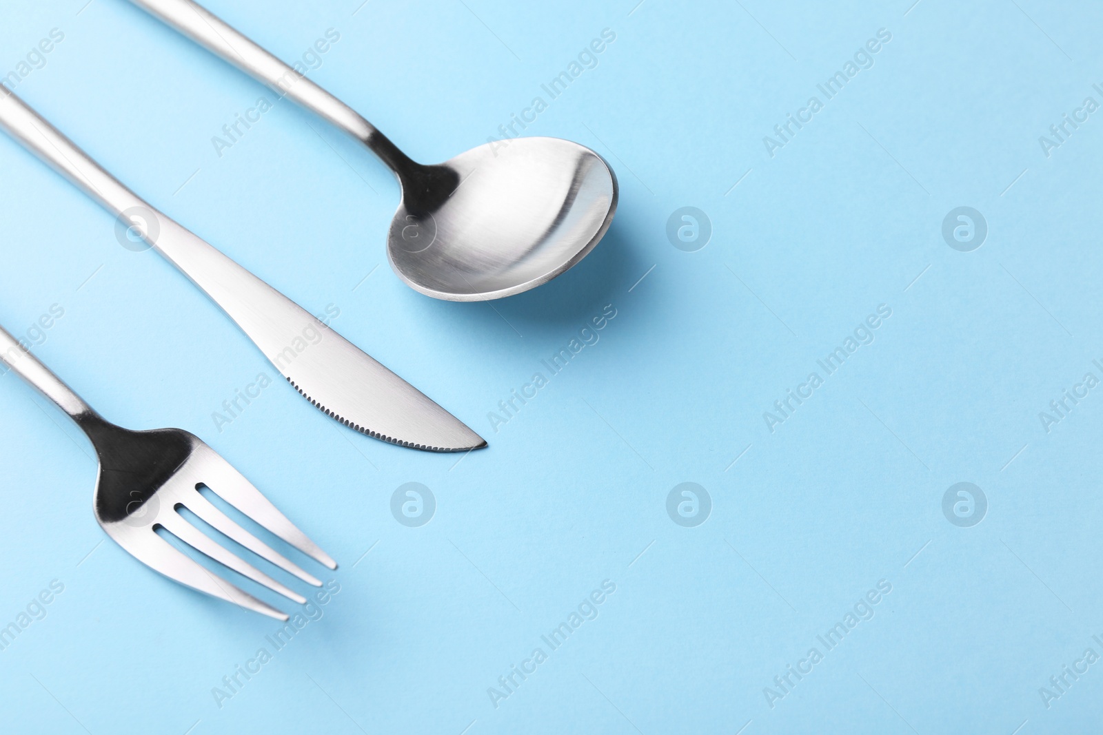 Photo of Stylish cutlery set on light blue table, closeup. Space for text