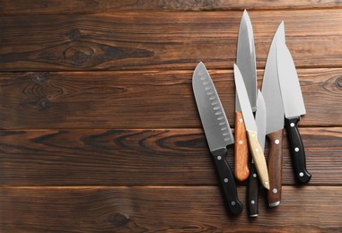 Photo of Many different knives on wooden table, flat lay. Space for text