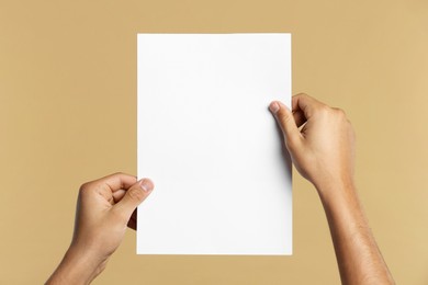 Photo of Man holding sheet of paper on beige background, closeup. Mockup for design