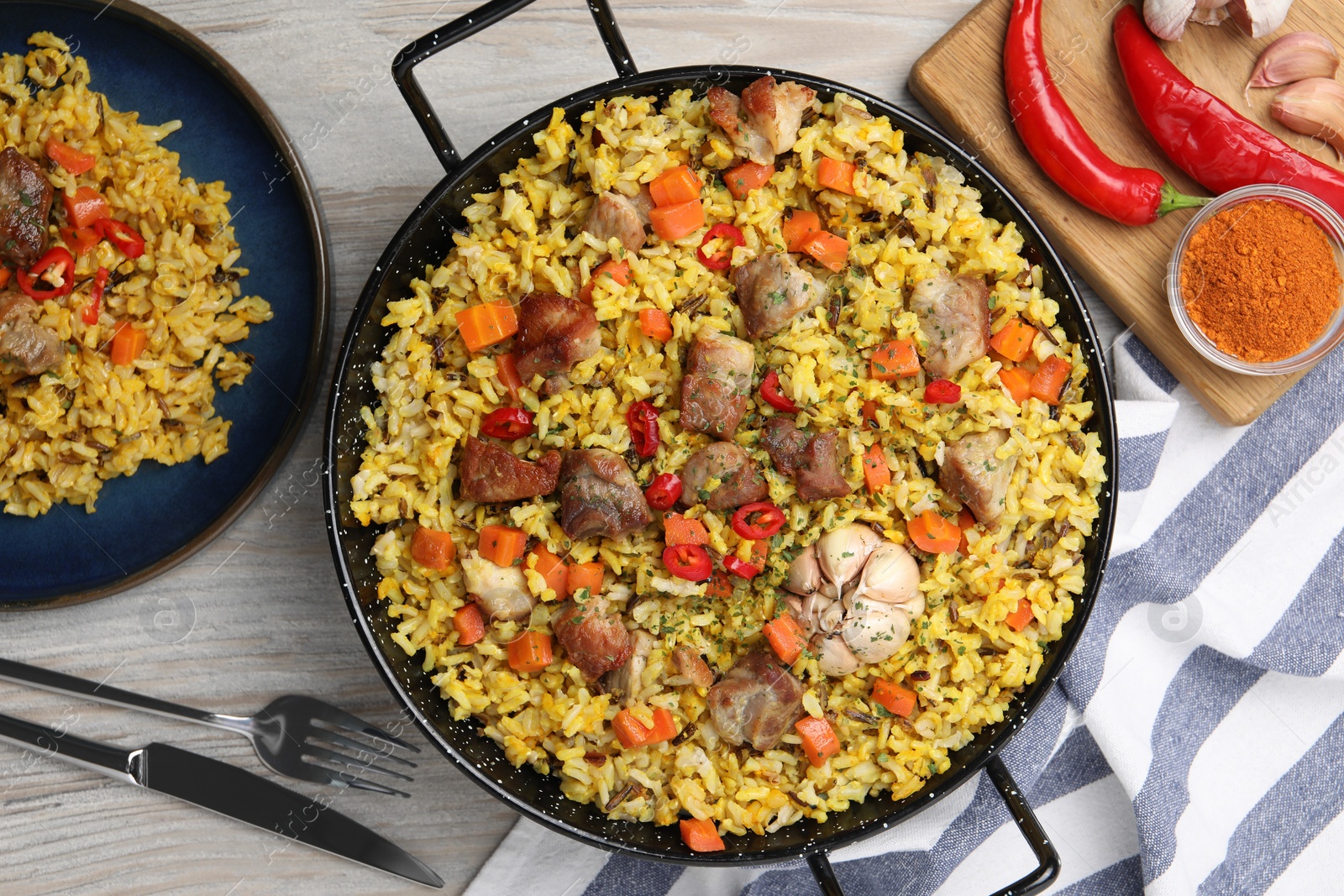 Photo of Delicious pilaf with meat, carrot and chili pepper served on wooden table, flat lay