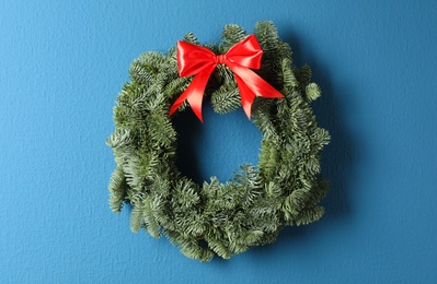 Christmas wreath made of fir tree branches with red ribbon on blue background