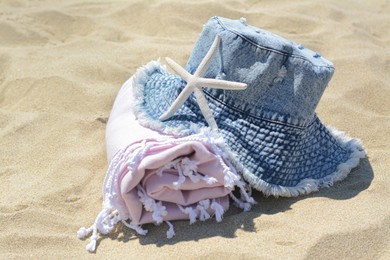 Photo of Stylish denim hat, blanket and starfish on sand outdoors. Beach accessories