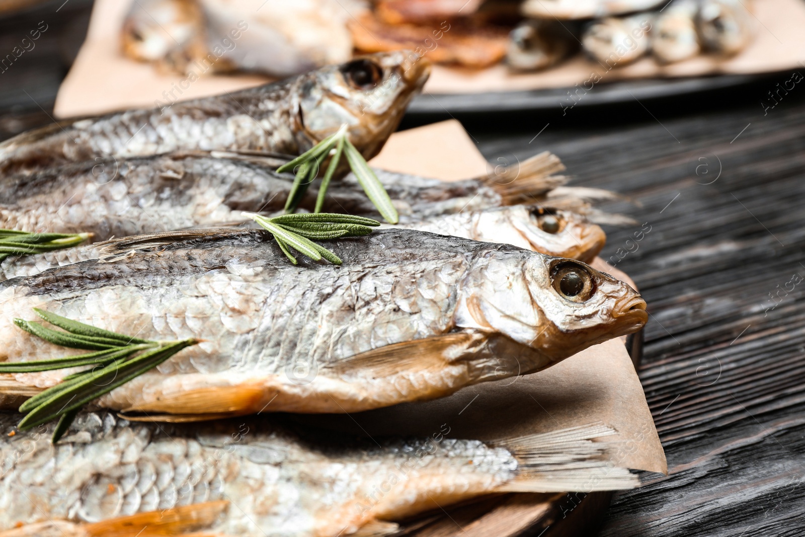 Photo of Tasty dried fish with rosemary on black wooden table, closeup