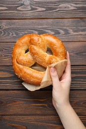 Photo of Woman with tasty freshly baked pretzel at wooden table, top view