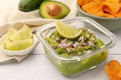 Photo of Bowl of delicious guacamole with onion and lime on white wooden table, closeup