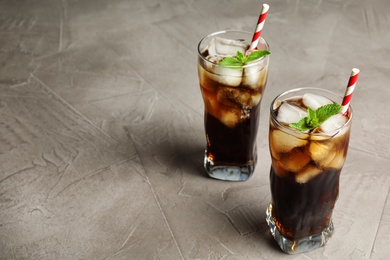 Photo of Glasses of refreshing soda drink with ice cubes and straws on grey table, space for text