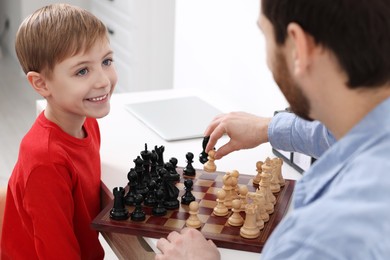 Photo of Father and son playing chess at table indoors, closeup