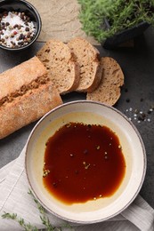 Photo of Bowl of balsamic vinegar with oil, spices and bread on dark grey table, flat lay