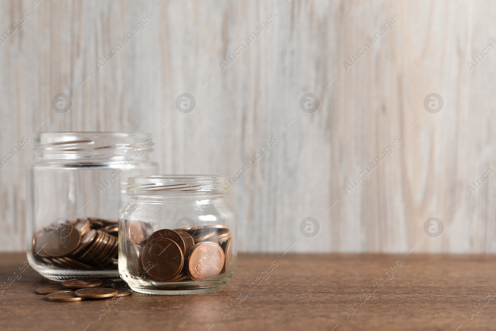 Photo of Glass jars with coins on wooden table. Space for text