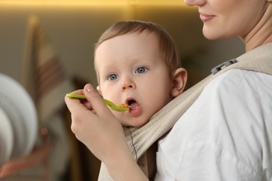 Photo of Mother feeding her cute child in sling (baby carrier) indoors