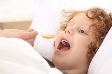 Photo of Mother giving cough syrup to her son on bed, closeup