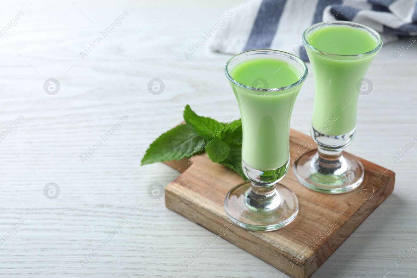 Photo of Delicious mint liqueur with green leaves on white wooden table. Space for text