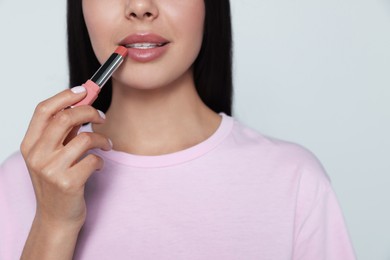 Young woman applying nude lipstick on gray background, closeup
