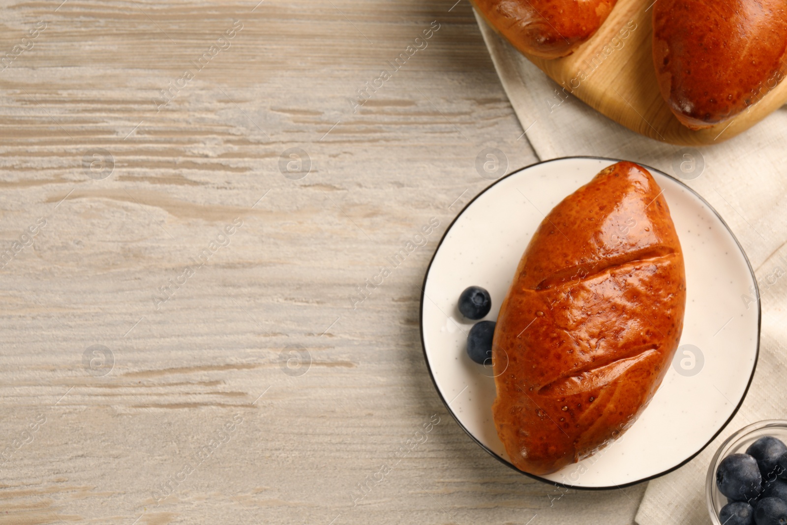 Photo of Delicious baked pirozhki and blueberries on wooden table, flat lay. Space for text