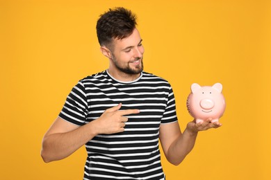 Photo of Happy young man with piggy bank on orange background