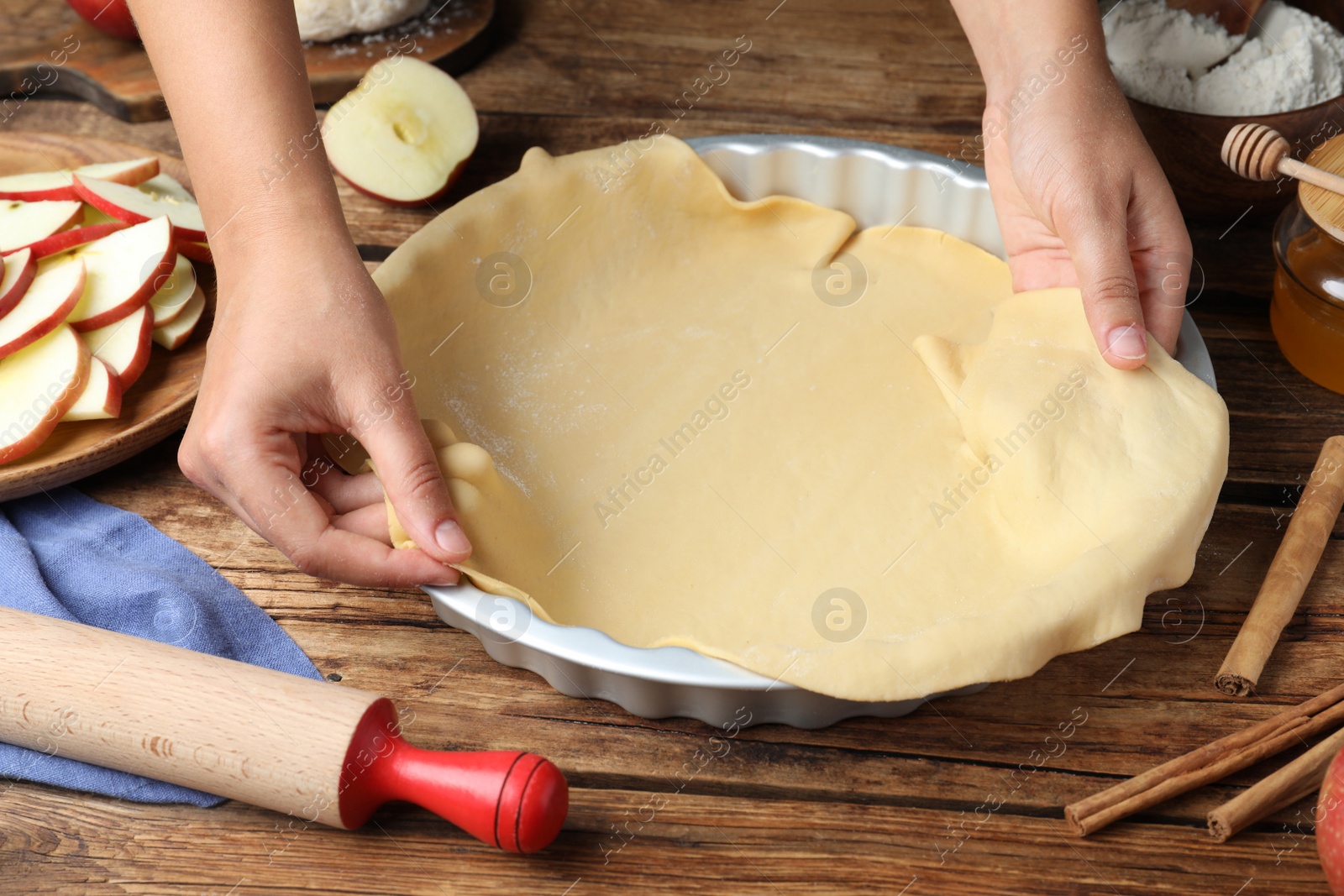 Photo of Woman putting dough for apple pie into baking dish at wooden table, closeup