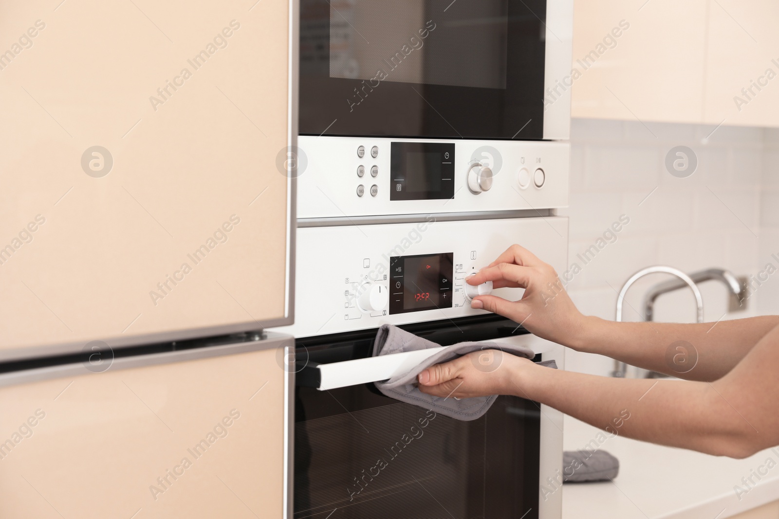 Photo of Woman adjusting electric oven in kitchen, closeup