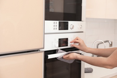 Photo of Woman adjusting electric oven in kitchen, closeup