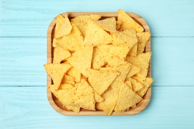 Wooden plate of tasty Mexican nachos chips on light blue wooden background, top view