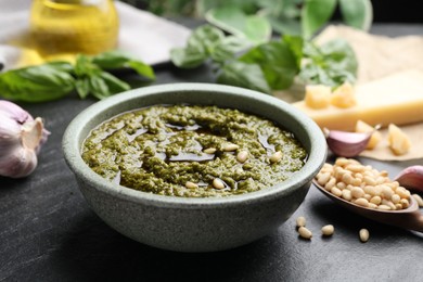 Photo of Tasty pesto sauce in bowl, pine nuts and garlic on black table, closeup