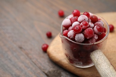 Photo of Frozen red cranberries in glass pot on wooden table, closeup. Space for text