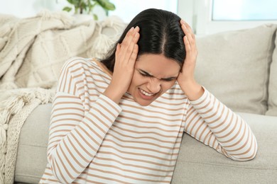 Photo of Young woman suffering from headache near sofa indoors. Hormonal disorders