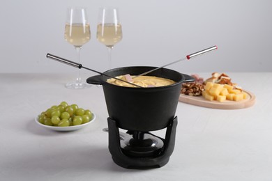 Photo of Fondue pot with tasty melted cheese, forks, wine and different snacks on white table
