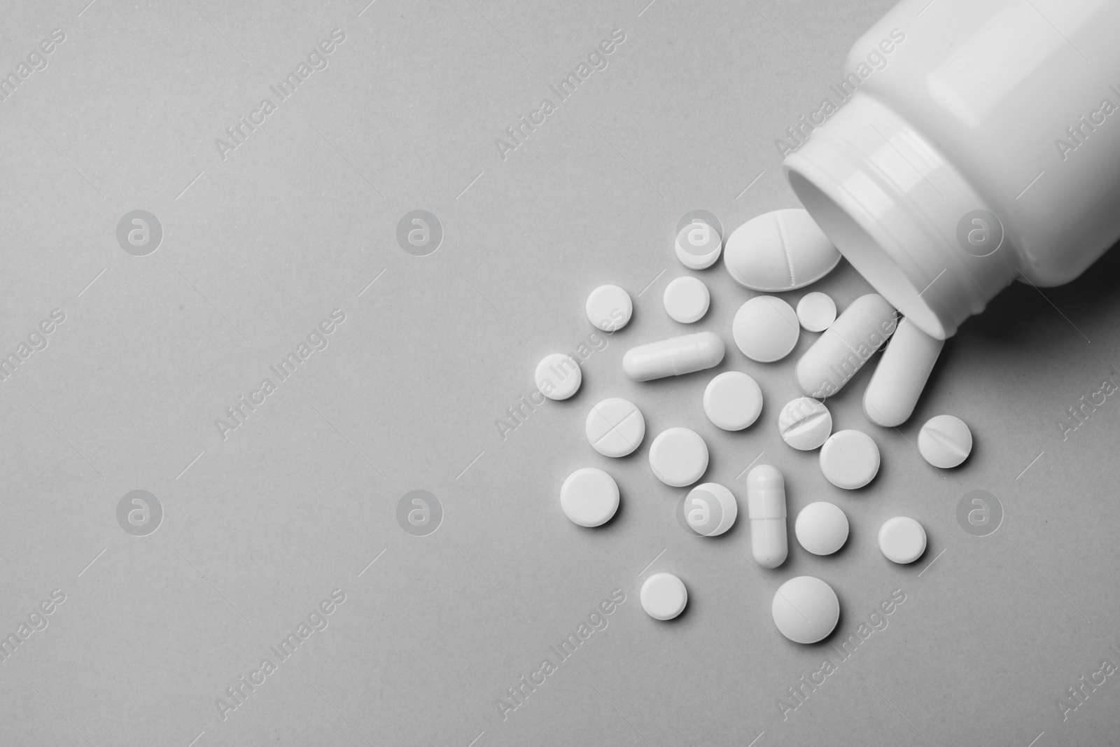 Photo of Bottle with different pills on grey background, flat lay. Space for text