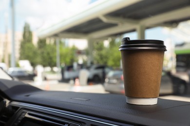 Paper coffee cup on car dashboard at gas station. Space for text