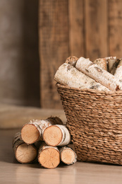 Photo of Wicker basket with cut firewood on floor indoors
