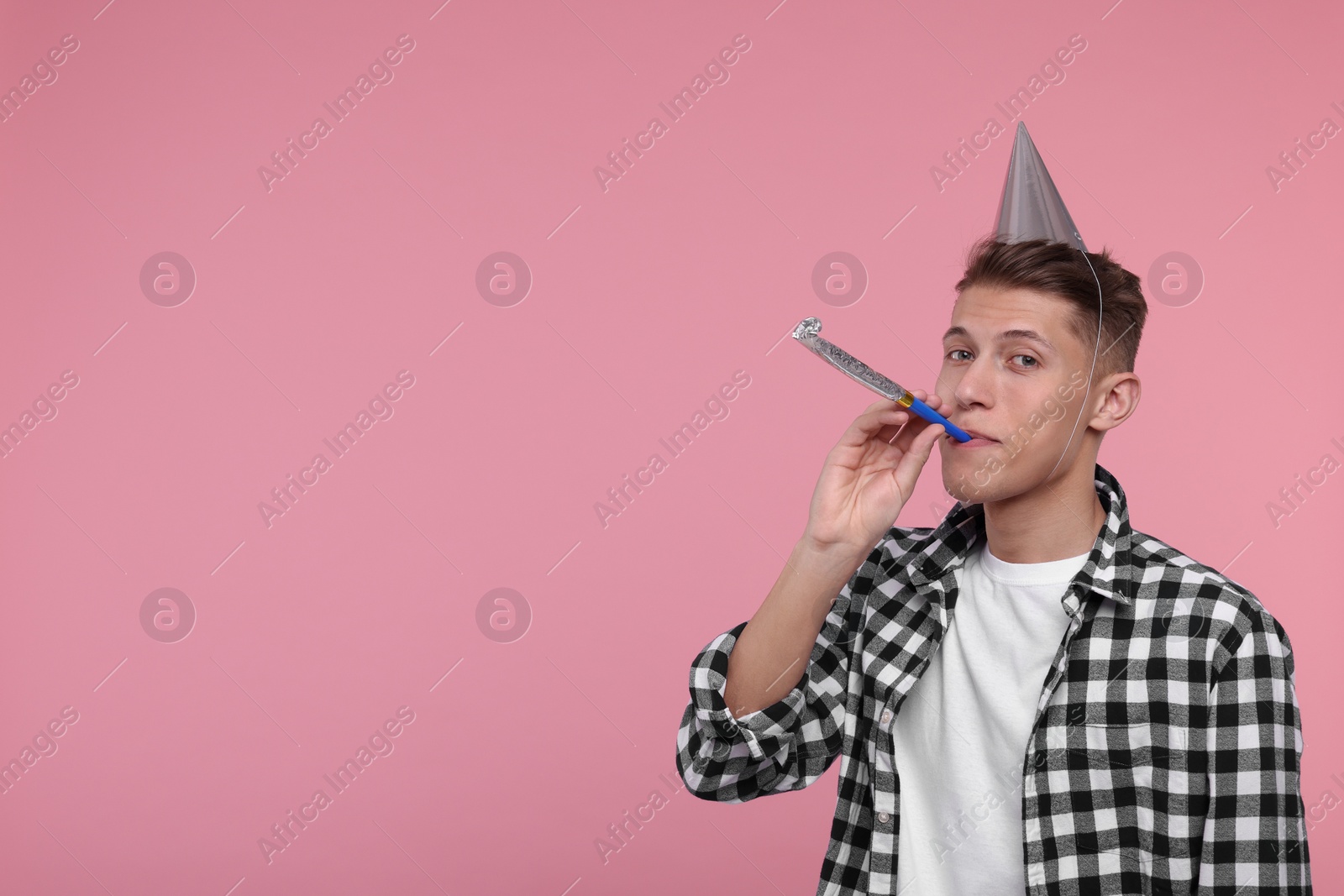 Photo of Young man in party hat with blower on pink background. Space for text