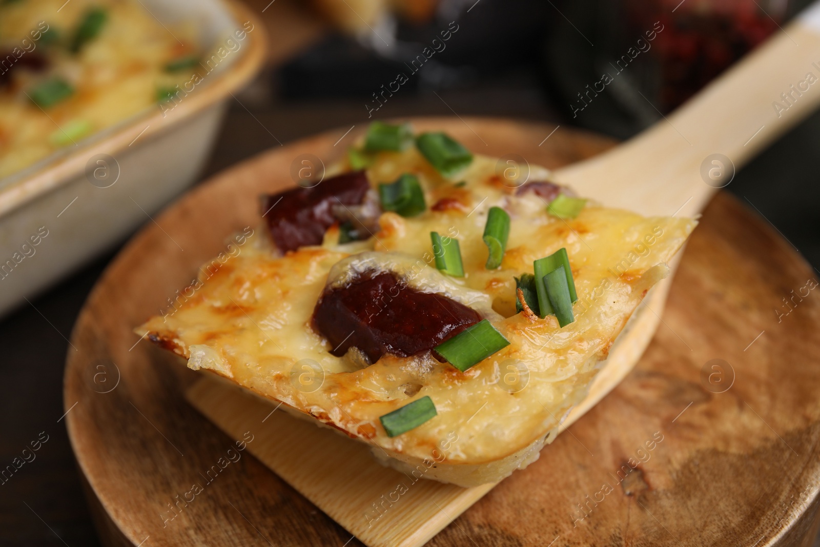 Photo of Spatula with piece of tasty sausage casserole on table, closeup