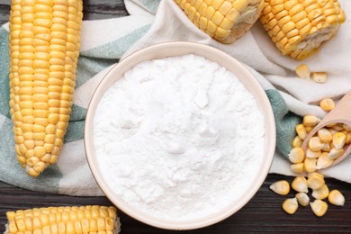 Photo of Bowl with corn starch, ripe cobs and kernels on dark wooden table, flat lay